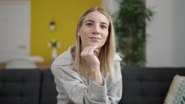 Young blonde woman smiling confident sitting on the sofa at home