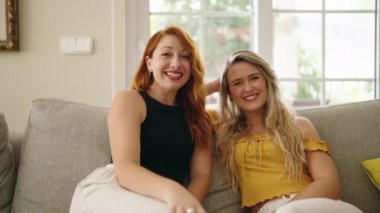 Two women sitting on sofa speaking at home