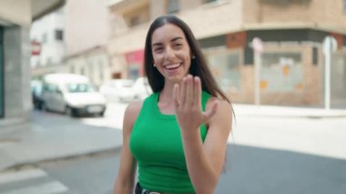 Genç, güzel İspanyol kadın gülümsüyor kendinden emin bir şekilde sokakta el kol geziyor.