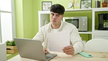Genç İspanyol adam yemek odasında dizüstü bilgisayar okuyarak stres ifadesi sergiliyor.