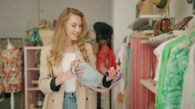 Giyim mağazasında el çantası takan genç sarışın kadın müşteri.