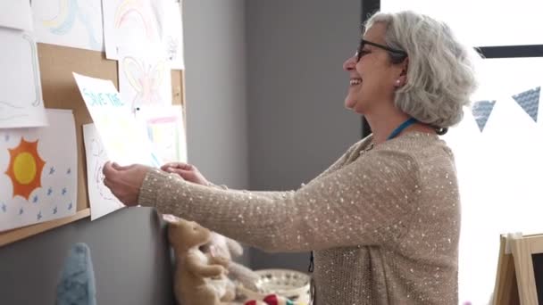 Frau Mittleren Alters Mit Grauen Haaren Erzieherin Hängt Zeichnung Korkbrett — Stockvideo