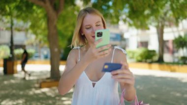 Parkta akıllı telefon ve kredi kartı kullanan genç sarışın kadın.