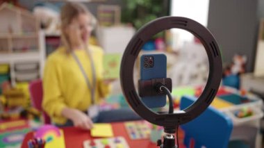 Young blonde woman preschool teacher recording vocabulary lesson at kindergarten
