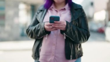 Genç ve cüsseli bir kadın sokakta akıllı telefon kullanarak gülümsüyor.