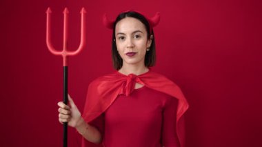 Şeytan kostümü giyen genç ve güzel bir İspanyol kadın izole edilmiş kırmızı arka planda mızrak taşıyor.
