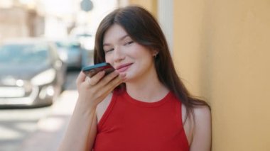 Beyaz bir kadın gülümsüyor ve caddede akıllı telefondan konuşuyor.