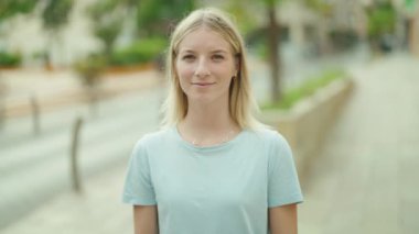 Genç sarışın kadın gülümsüyor. Kendinden emin. Sokakta el kol hareketi yapıyor.