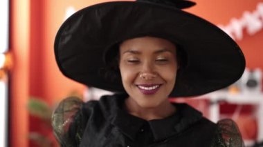 African american woman wearing witch costume having halloween party at home