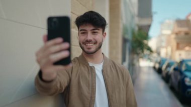 Young hispanic man smiling confident having video call at street