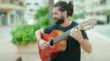 Young hispanic man musician playing classical guitar at park