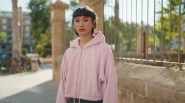 Genç İspanyol kadın gülümsüyor. Kollarını kavuşturup caddede duruyor.