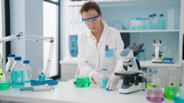Laboratuvarda sıvı ölçen orta yaşlı kadın bilim adamı üniforması giyiyor.