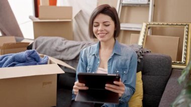 Genç beyaz kadın yeni evinde tablet kullanarak gülümsüyor.