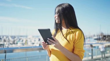 Deniz kenarında dokunmatik ped kullanan güzel İspanyol kadın gülümsüyor.