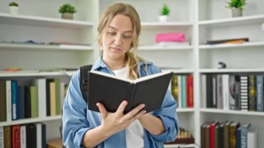 Kütüphanede kitap okuyan sarışın genç bir kız öğrenci.
