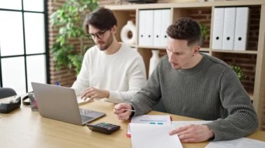 Ofiste dizüstü bilgisayar kullanan iki erkek iş ortağı.