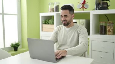 Young hispanic man using laptop dancing at home