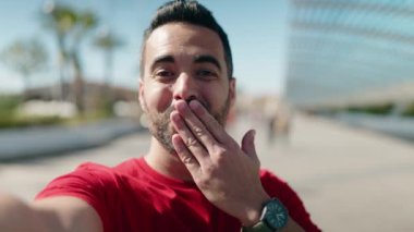 Genç İspanyol adam gülümsüyor. Sokakta akıllı telefonun yanında özçekim yapıyor.