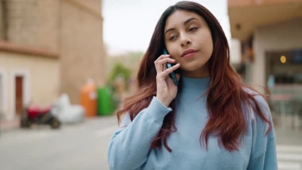 若いヒスパニック系の女性が路上でスマートフォンで自信を持って話して笑顔 — ストック動画