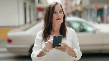 Genç, güzel, İspanyol bir kadın sokakta akıllı telefon kullanarak gülümsüyor.
