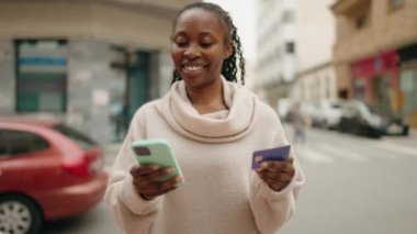 African american woman using smartphone and credit card at street