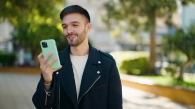 Genç İspanyol adam gülümsüyor. Parkta kendine güvenen bir video çağrısı var.
