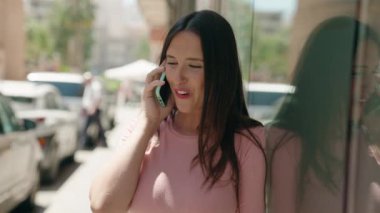 Genç, güzel, İspanyol bir kadın gülümsüyor ve caddede akıllı telefondan konuşuyor.