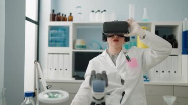 Young redhead woman wearing scientist uniform using virtual reality glasses working at laboratory