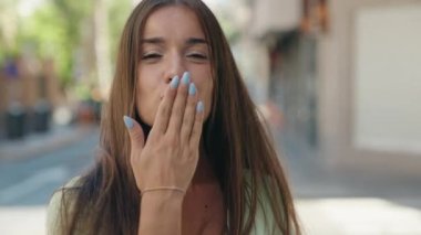 Young beautiful hispanic woman smiling confident doing kiss gesture with hand at street