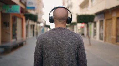 Genç kel adam sokakta müzik dinliyor.