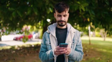 Parkta akıllı telefon kullanarak gülümseyen İspanyol genç adam.