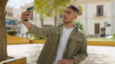 Genç İspanyol adam gülümsüyor. Parktaki akıllı telefonun yanında özçekim yapıyor.