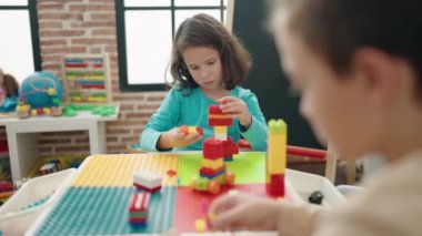 Group of kids playing with construction blocks sitting on table at kindergarten
