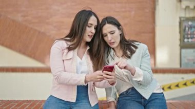 Sokakta akıllı telefon kullanan kendine güvenen iki kadın.