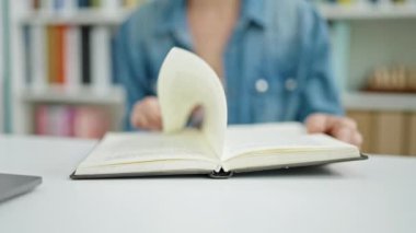 Üniversite sınıfında masa başında oturmuş kitap okuyan beyaz bir kadın.