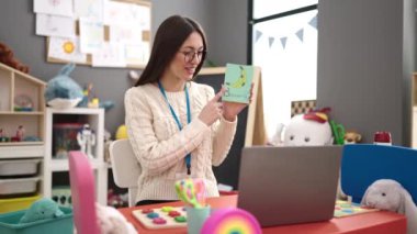 Young beautiful hispanic woman preschool teacher having online vocabulary lesson at kindergarten