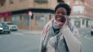 Genç Afrikalı Amerikalı kadın gülümsüyor. Kendine güveni tam. Sokakta akıllı telefondan konuşuyor.