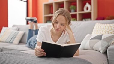 Kitap okuyan genç sarışın kadın evdeki kanepede yatmaktan yoruldu.