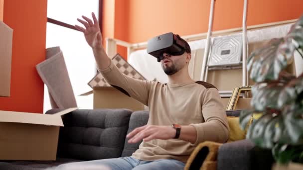 若いですArab男座っています上のソファ使用して仮想現実眼鏡で新しい家 — ストック動画