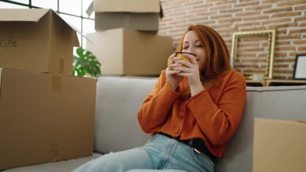 Молодая Рыжая Женщина Пьет Кофе Сидя Диване Новом Доме — стоковое видео