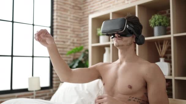 年轻的惊慌失措的男人坐在床上 卧室里戴着一副虚拟现实眼镜 — 图库视频影像