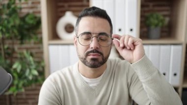 Young hispanic man business worker smiling confident sitting on table at office
