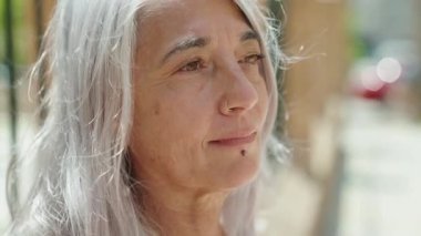 Middle age grey-haired woman smiling confident looking to the side at street
