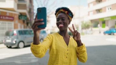 Genç Afrikalı Amerikalı kadın gülümsüyor. Kendine güveni tam. Sokakta akıllı telefondan selfie çekiyor.