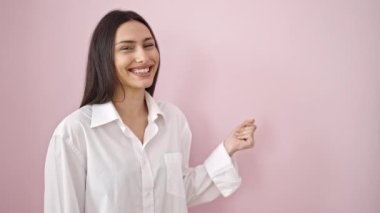 Genç, güzel İspanyol kadın gülümsüyor, kendine güveni tam, pembe arka planda, parmak üstüne parmak işareti yapıyor.