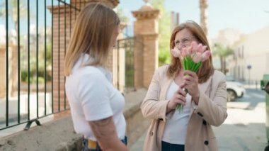 Mother and daughter hugging each other holding bouquet of flowers at street