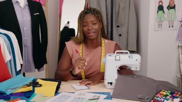 非洲裔美国妇女裁缝笑着在裁缝店的笔记本上自信地写作 — 图库视频影像