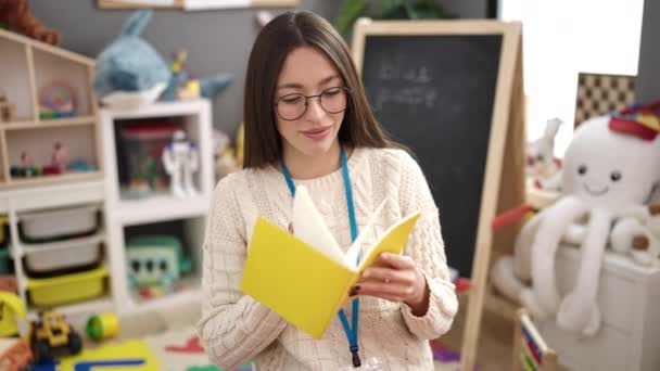 Young Beautiful Hispanic Woman Preschool Teacher Reading Book Standing Kindergarten — Vídeo de Stock