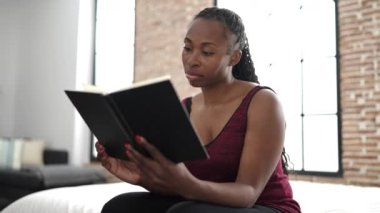 Afrikalı kadın kitap okuyor. Yatak odasında oturuyor.